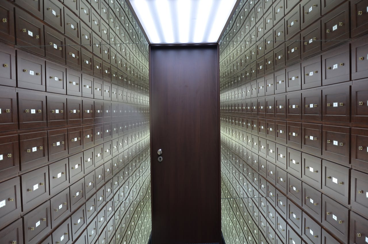 services-04 Wooden lockboxes line the walls of a modern, secure vault with a central wooden door.