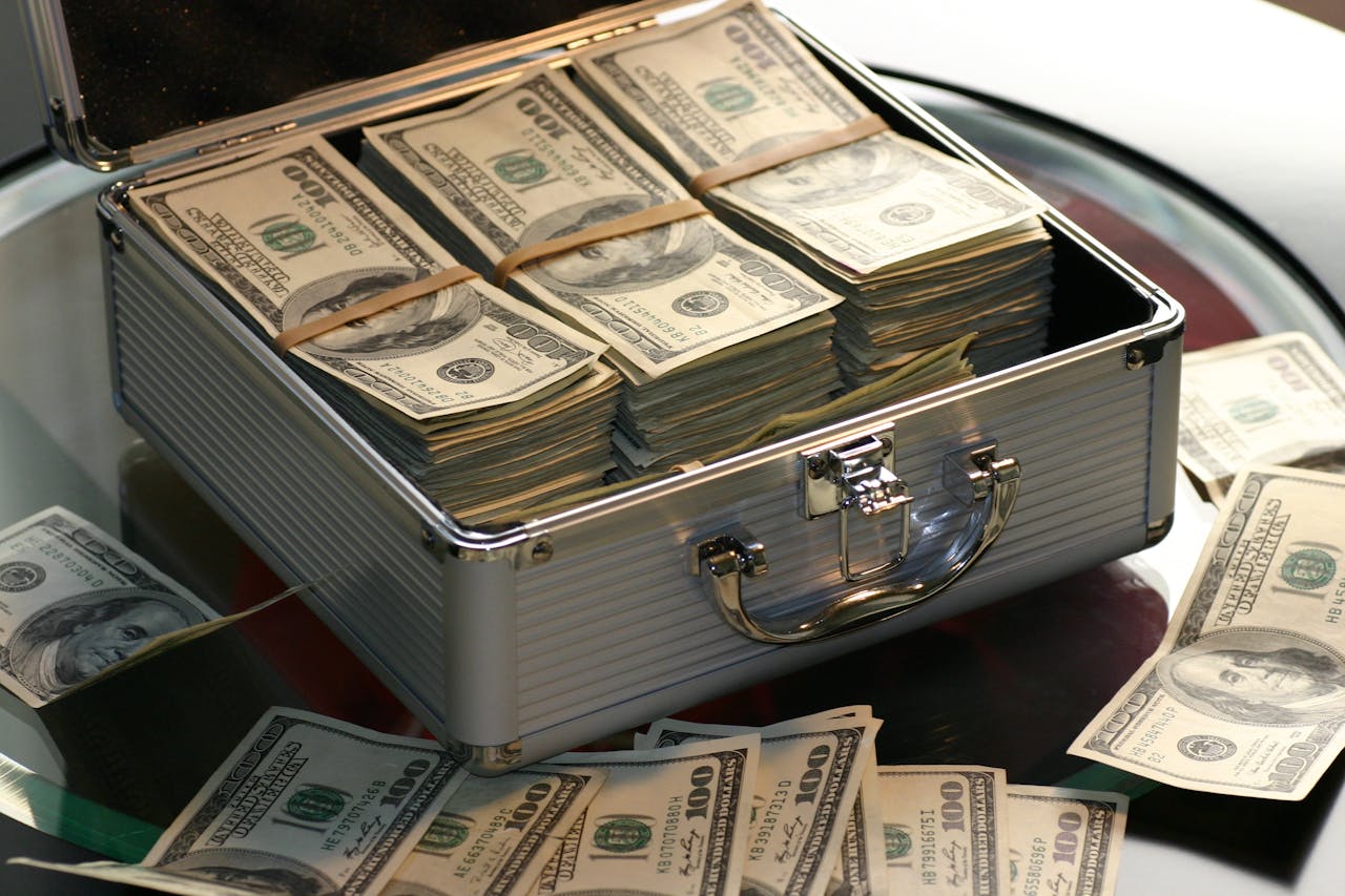 services-01 Open briefcase filled with stacks of hundred dollar bills on a glass table, representing wealth.