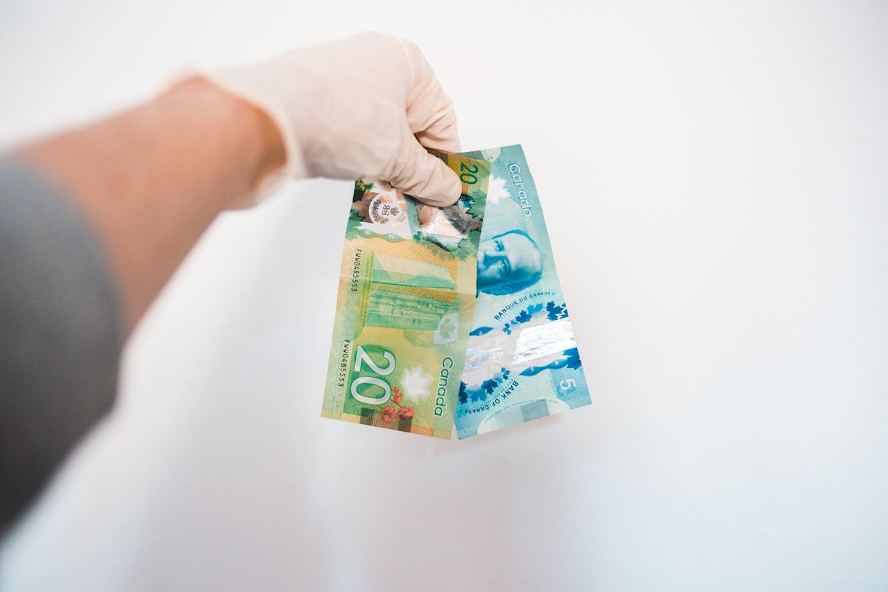 team-02 Crop anonymous male in sterile glove demonstrating different paper bills with image of President and colorful illustrations with numbers near white wall at home