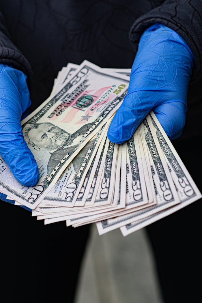 team-05 Hands in protective gloves holding multiple US dollar bills, symbolizing virus protection and financial transactions.