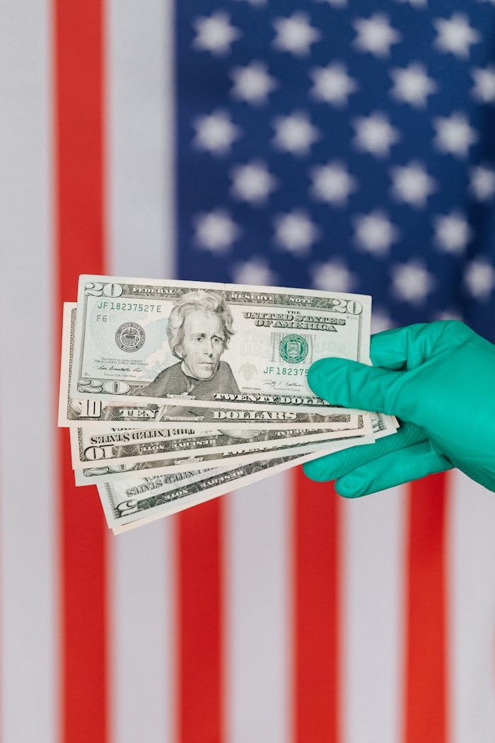 team-03 Unrecognizable person in medical disposable gloves demonstrating paper banknotes against multicolored American flag on background